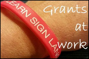 Grants, with a photo of a wrist bracelet reading learn sign language